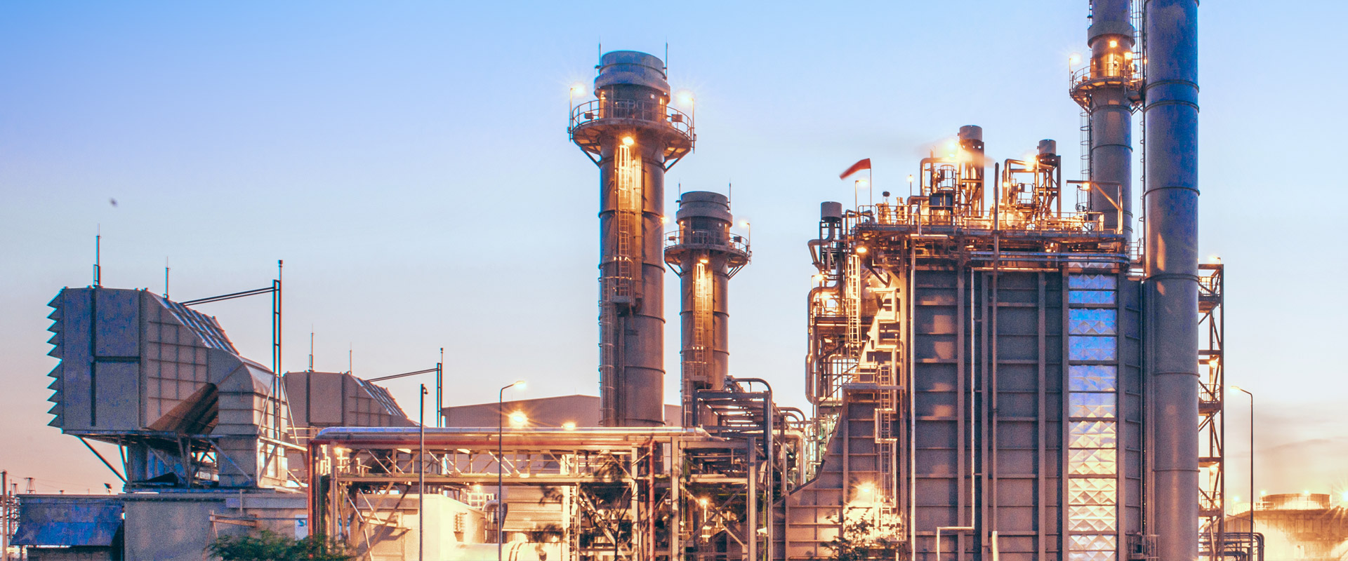 Industrieanlage mit beleuchteten Rohrleitungen und Türmen in der Abenddämmerung