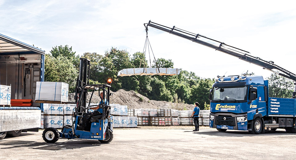 Ladekran hebt Baumaterial von einem LKW auf einer Baustelle