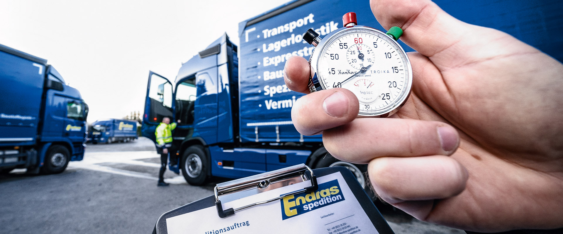 Eine Hand hält eine Stoppuhr vor einem blauen Endras-Lkw