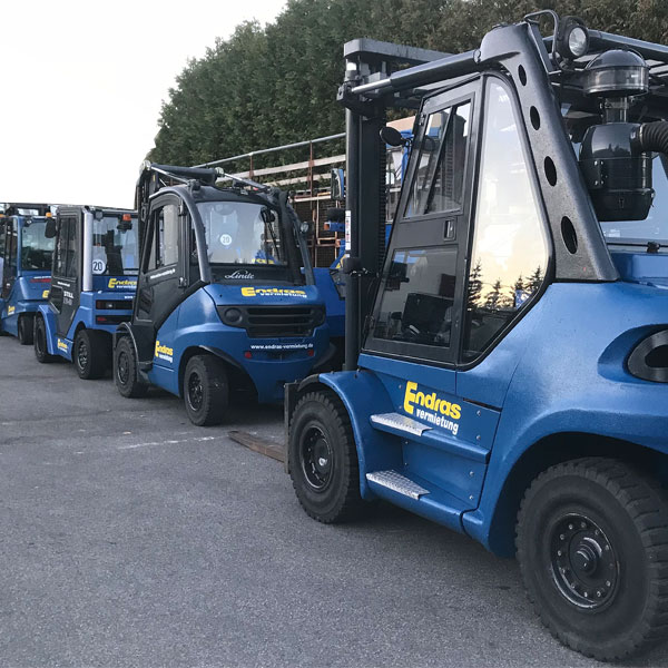 Mehrere blaue Gabelstapler stehen aufgereiht auf dem Betriebshof