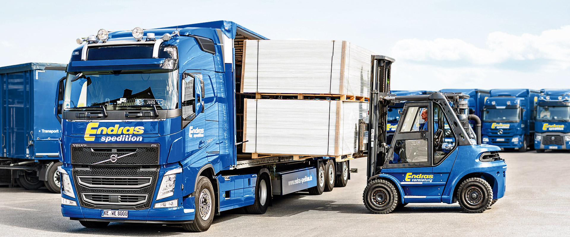 Ein Stapler belädt einen Endras-Sattelzug mit Plattenware, dahinter weitere Lkw des Fuhrparks