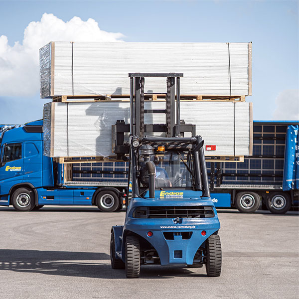 Ein Gabelstapler transportiert gestapelte, verpackte Ware vor zwei Endras-Lkw